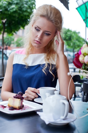 a beautiful young blond girl in summer dress at the table in pavement cafe is having a headacheの写真素材