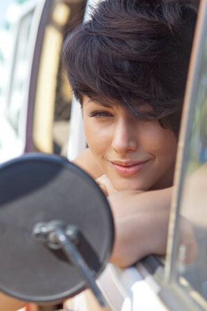 a beautiful young girl with short hair cut and blue eyes is looking into the side view mirror  の写真素材