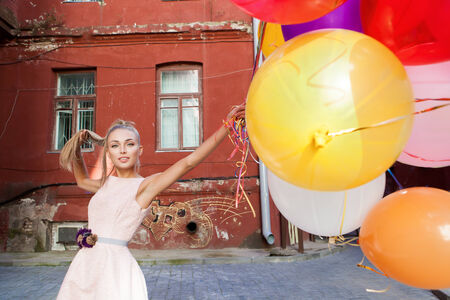 beautiful happy girl in pink dress holding a bunch of balloons sets her hairの写真素材