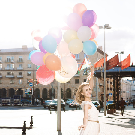 beautiful blonde girl with long legs in summer dress holds a bunch of multicolored balloonsの写真素材