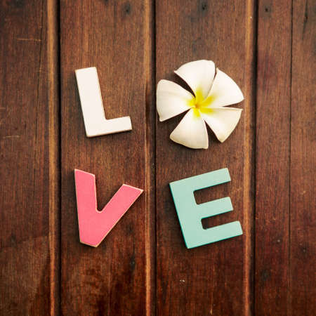 word love made up of colorful wooden letters with white and yellow frangipani flower instead of...