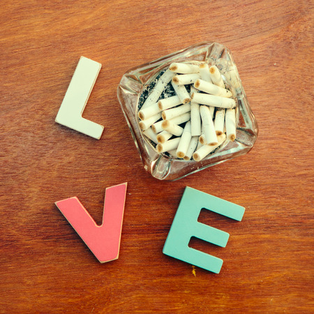 word love made up of colorful wooden letters with dirty ashtray full of butts and ash instead of letter O on a wooden table. February 14, Valentineの写真素材