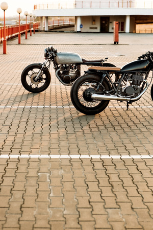 Two sexy vintage custom motorcycles cafe racer looking in opposite directions on empty rooftop parking lot with during sunset. Symbol of wild ride, straight road, urban style, hipster lifestyle.の写真素材