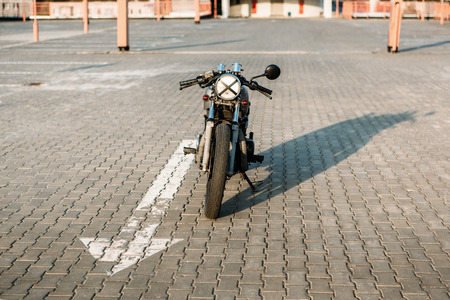 Front view on silver vintage custom motorcycle motorbike caferacer on empty rooftop parking lot at city center surrounded by urban environments midtown buildings. Hipster lifestyle.の写真素材