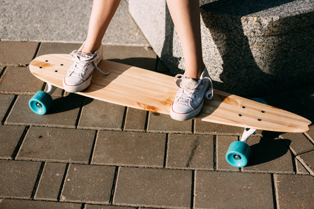 Close up of woman leg in white sneakers resting after extreme funny ride her wooden longboard skateboard. Modern urban hipster girl have fun. Good sunny summer day for skateboarding and have fun.の写真素材