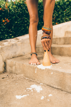 Close up of tragedy, bad day, negative emotions. Girl drop ice cream cone on her feet on the stone stairs in tropical house resort and want to take it up. Outdoor lifestyle on hot sunny summer day.の写真素材