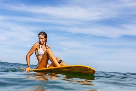Beautiful fit surfing lady in sexy bikini doing yoga on big longboard surf surfboard board on sunrise or sunset in the ocean and try to find balance. Modern active sport lifestyle and summer vacation.の写真素材