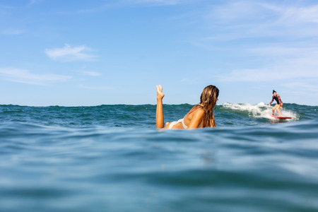 Two beautiful fit surfing girl in sexy bikini on surf surfboard board on sunrise or sunset in the ocean. Woman look how her friend ride good wave. Modern active sport lifestyle and summer vacation.の写真素材
