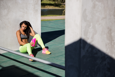 Beautiful young girl with long legs in bright sexy leggings with pretty athlete muscular body sit with protein shaker. Crossfit training urban area street gym city exercise routine healthy lifestyle.の写真素材