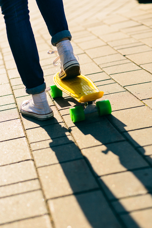 Close up of fit woman in jeans and white sneakers ready to ride her penny board skateboard in sunset light. Modern urban hipster girl have fun. Good sunny summer day for skateboarding and have fun.の写真素材