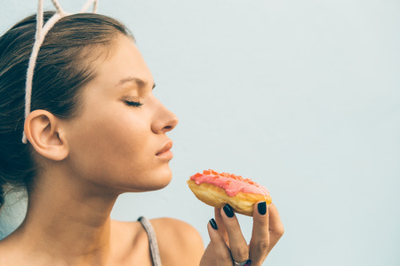 Close up of sexy slim girl eat tasty sweet heart shaped donut. Beauty cute girl in a tropical resort. Outdoor lifestyle portrait on hot sunny summer day. Concept of love, feelings, positive emotions.の写真素材