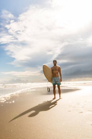 Out of focus, blurry image of handsome boy with surfing surf board walk from water at surf spot at...
