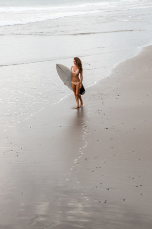 Surf girl with long hair go to surfing. Sexy surfer woman holding blank white short surfboard on a beach at sunset or sunrise. Bali island, Indonesia. Outdoor Active Lifestyle. It's time for surfing!の写真素材