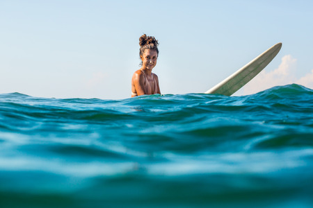 Beautiful young brunette girl in a bikini swimsuit look to camera. Sporty surfer woman surfing in...