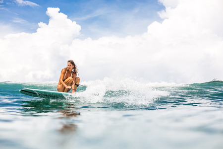 Beautiful young surfer lady in sexy pink bikini surfing longboard on the big waves in the open ocean. Modern family lifestyle, people water sport adventure camp and extreme swim on summer vacation.の写真素材