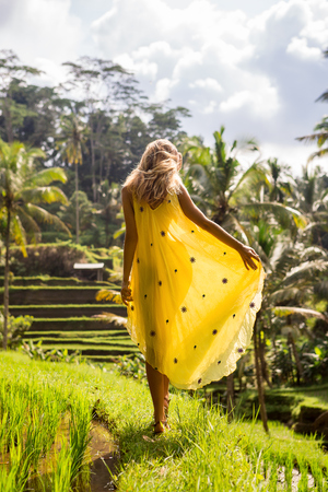 Beautiful young woman in yellow silk dress. Girl travel and explore world. Typical Asian hillside with rice farming, mountain shape green cascade rice field terraces paddies. Ubud, Bali, Indonesia.の写真素材