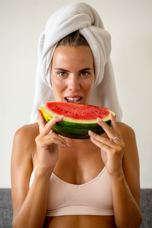 Portrait of beautiful cute woman in sexy lingerie with white towel on head eat slice of juicy red watermelon. Healthy eating lifestyle concept. Health care and beauty. Fitness food. Proper nutrition.の写真素材
