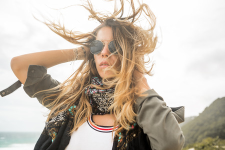 Hipster woman in fashion khaki shirt vogue scarf and vintage sunglasses correct her long hairs on the wind . Modern tourist traveler, active lifestyle, sport adventure camp and extreme on vacation.の写真素材