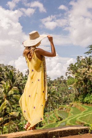 Beautiful young lady in vogue dress and straw hat. Girl travel and enjoy typical Asian hillside with rice farming, mountain shape green cascade rice field terraces paddies. Ubud, Bali, Indonesia.の写真素材