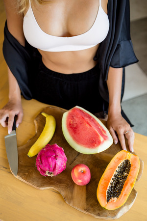 Sexy lady with tasty fruits on a kitchen. Papaya, Carica, apple, watermelon, dragon fruit. Healthy eating lifestyle concept. Health care and beauty. Healthy breakfast. Fitness food. Proper nutrition.の写真素材
