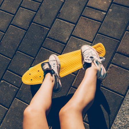 Close up of long girl leg in white sneakers resting after extreme funny ride her penny board skateboard. Modern urban hipster girl have fun. Good sunny summer day for skateboarding and have fun.の写真素材