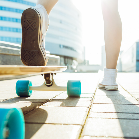 Close up of sporty lady in white sneakers ready to extreme funny ride her wooden skate longboard skateboard in sun light. Modern urban hipster girl have fun. Good sunny summer day for skateboarding.の写真素材
