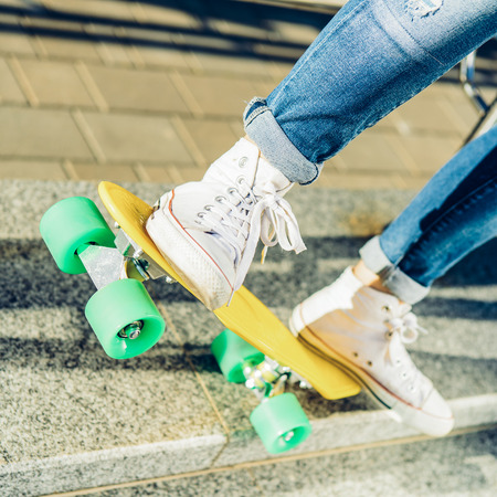 Close up of sport lady's legs in jeans and white sneakers on penny board skateboard. Modern urban hipster girl have fun. Good sunny summer day for lifestyle skateboarding and have fun.の写真素材