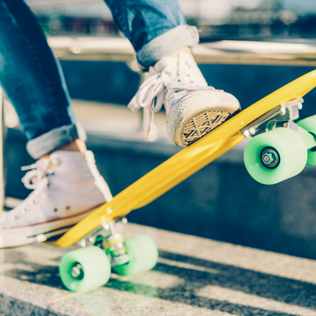 Close up of sport lady's legs in jeans and white sneakers extremely ride penny board skateboard. Modern urban hipster girl have fun. Good sunny summer day for lifestyle skateboarding and have fun.の写真素材