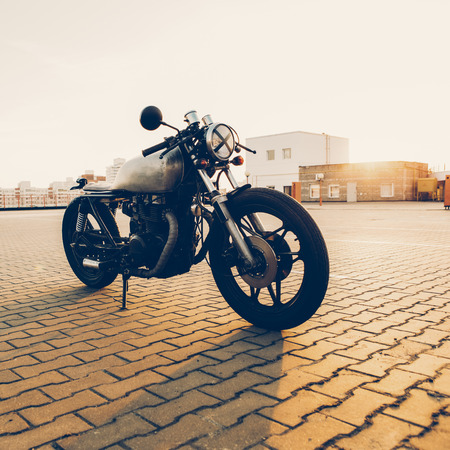 Brutal custom vintage motorbike cafe racer sexy motorcycle with raw metal gas tank and tape cross over optic at headlamp on empty rooftop parking lot during sunset. Hipster lifestyle, student dream.の写真素材