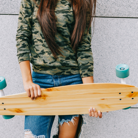 Portrait of happy beautiful brunette woman with long sexy healthy hair hold her wooden longboard skateboard in front of her, look to the camera and smile. Urban scene, city life. Hipster cute lady.の写真素材