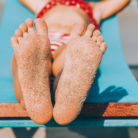 Cute little kid in red swimsuit and sunglasses enjoying on a sun lounger rest on the beach chair on...