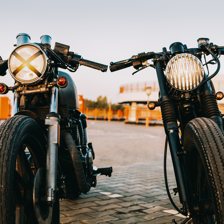 Two vintage custom motorbike cafe racer one with grill headlight another with tape cross over optic on empty rooftop parking lot during sunset. Hipster lifestyle. Lamp is on and directed to camera.の写真素材