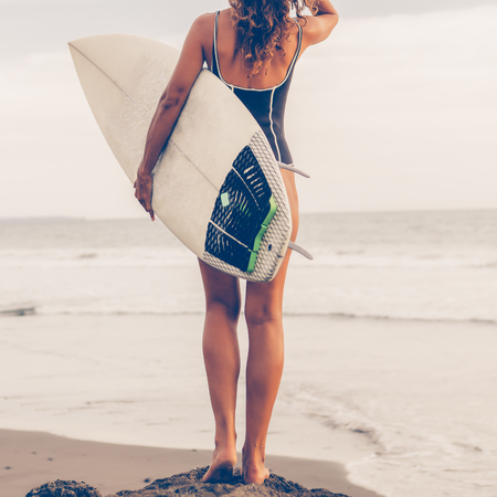 Surf girl with long hair go to surfing. Young surfer woman holding blank white short surfboard on a rock at sunset or sunrise. Bali island, Indonesia. Outdoor Active Lifestyle. It's time for surfing!の写真素材