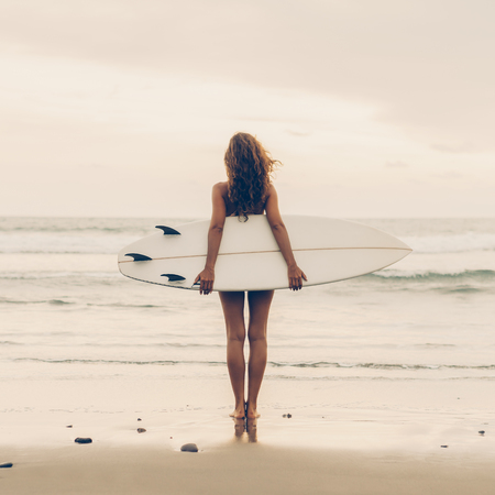 Surf girl with long hair go to surfing. Young surfer woman holding blank white short surfboard on a beach at sunset or sunrise. Bali island, Indonesia. Outdoor Active Lifestyle. It's time for surfing!の写真素材