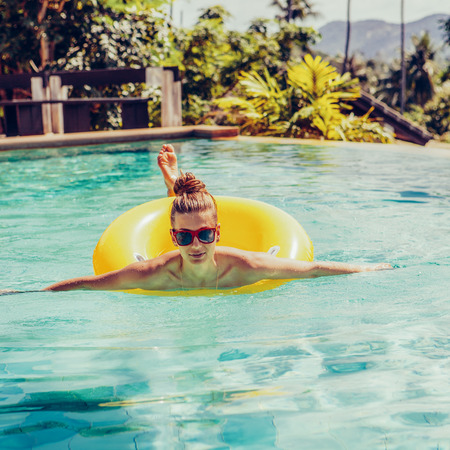 Amazing beautiful woman in sunglasses have fun in swimming pool. Outdoor lifestyle portrait of hipster girl wearing trendy swimsuit enjoying summer holidays, swimming with inflatable yellow ring.の写真素材