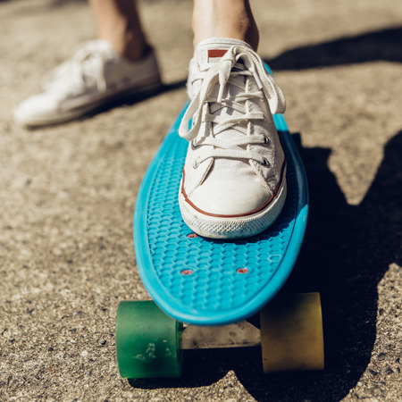 Closeup of feet of a beautiful woman in white sneakers rides on blue penny skate board longboard with multi colored wheels. Urban scene, city life. Sport, fitness lifestyle. Cute hipster have fun.の写真素材