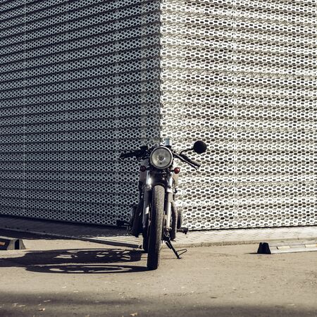 Vintage motorcycle parking near wall of finance building. Everything is ready for having fun after hard day in office. Modern young businessman hipster hobby. Space for your individual text.の写真素材