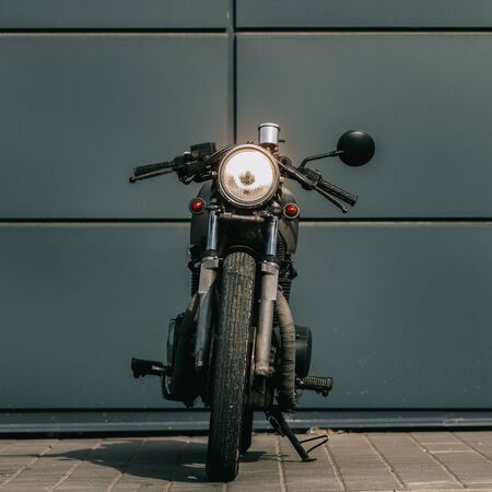 Vintage motorbike parking near gray wall of finance building. Everything is ready for having fun driving the empty road on a motorcycle tour journey. Businessman hobby. Space for your individual text.の写真素材