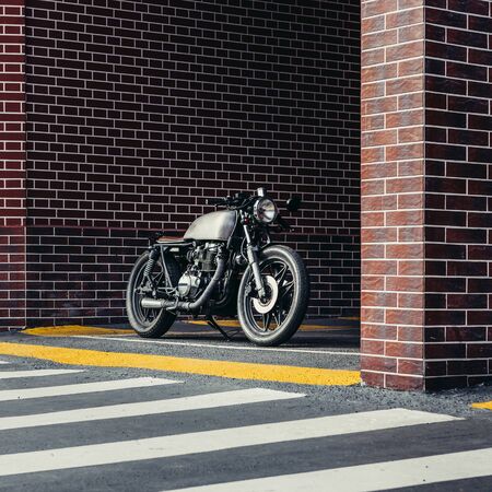 Handmade motorcyle parking near brick wall of industrial building. Everything is ready for having fun after hard day in office. Businessman city hipster hobby. Space for your individual text.の写真素材