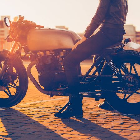 Sexy biker woman in black leather jacket and full face helmet sit on vintage custom caferacer motorcycle. Urban roof parking, sunset in big city. Traveling and active hipster lifestyle. Girls power.の写真素材