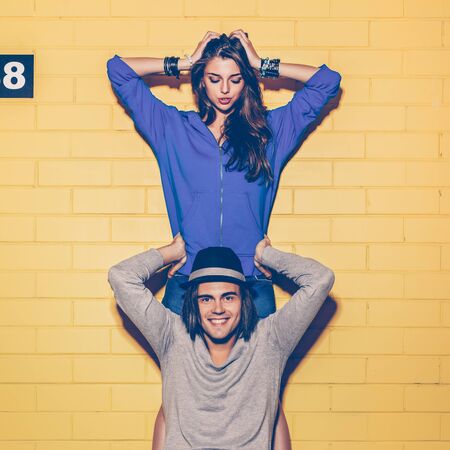Young modern happy couple in love having fun in front of yellow brick wall. Beautiful longhaired...