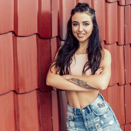 Portrait of athletic young cute woman in denim shorts, pink top and fashion hair style smiling and have good time. Urban style, healthy girl lifestyle and sport concept. Hipster city life.の写真素材