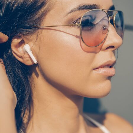 Close up portrait of athletic young cute woman in vogue sport suit correct her wireless sound earpods music headphones. Urban style, healthy girl lifestyle and sport concept. Hipster city life.の写真素材