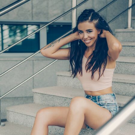 Close up portrait of athletic young cute lady in denim shorts, pink top and fashion hair style smiling and have good time. Urban style, healthy girl lifestyle and sport concept. Hipster city life.の写真素材