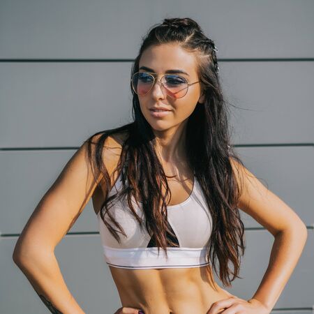 Close up portrait of athletic young cute female in vogue sport suit with fashion hair style smiling and posing to camera. Urban style, healthy girl lifestyle and sport concept. Hipster city life.の写真素材