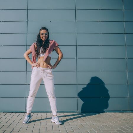 Close up portrait of athletic young cute woman in vogue sport suit with fashion hair style smiling and posing to camera. Urban style, healthy girl lifestyle and sport concept. Hipster city life.の写真素材