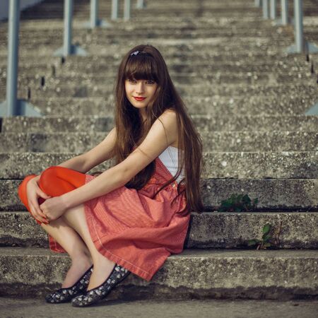 A beautiful girl with long hair coquettishly smiling. Young modern city woman look to the camera. Urban lifestyle holidays.の写真素材