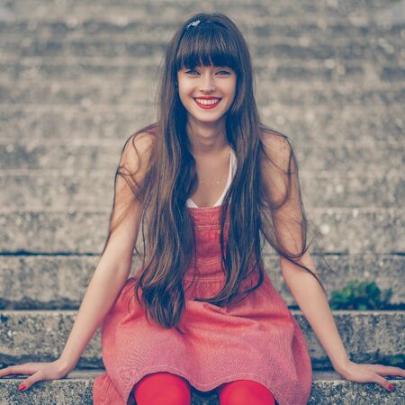 A beautiful girl with long hair coquettishly smiling. Young modern city woman look to the camera. Urban lifestyle holidays.の写真素材