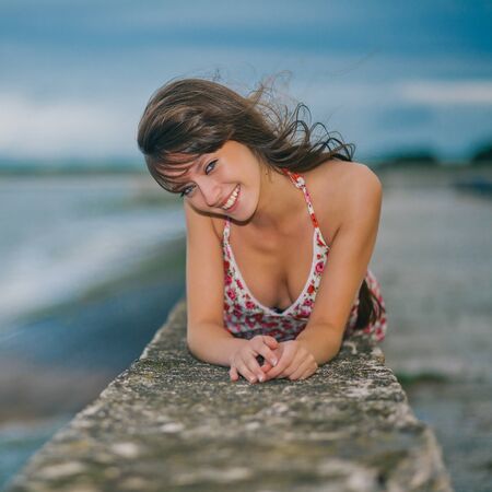 Beautiful girl in a light dress lying on a stone pierの写真素材