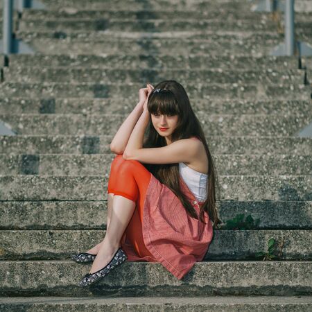 A beautiful girl with long hair coquettishly smiling. Young modern city woman look to the camera. Urban lifestyle holidays.の写真素材